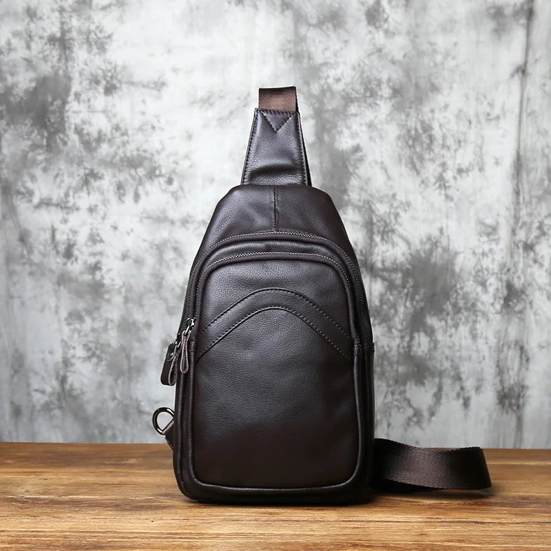 Brown leather sling bag on a wooden surface with a gray textured background