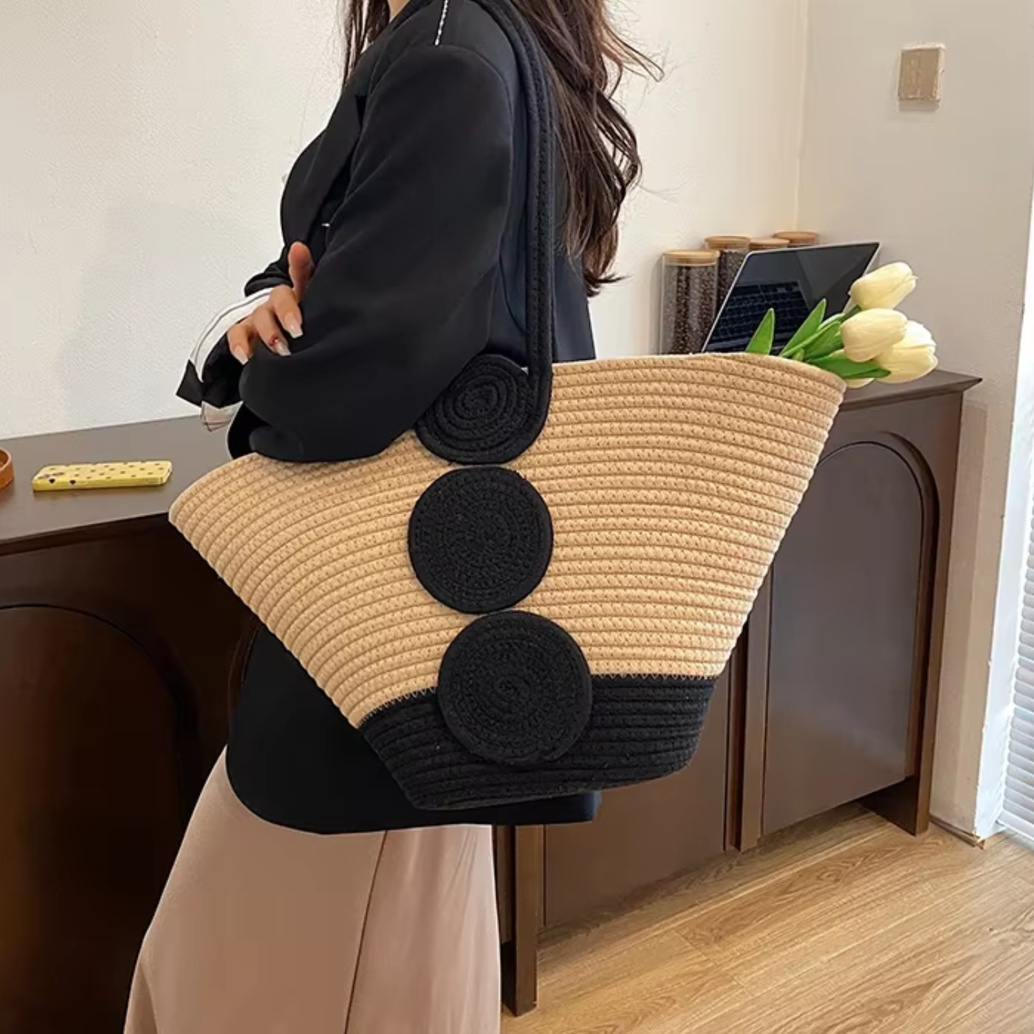 Person holding a large beige and black handbag in an indoor setting.