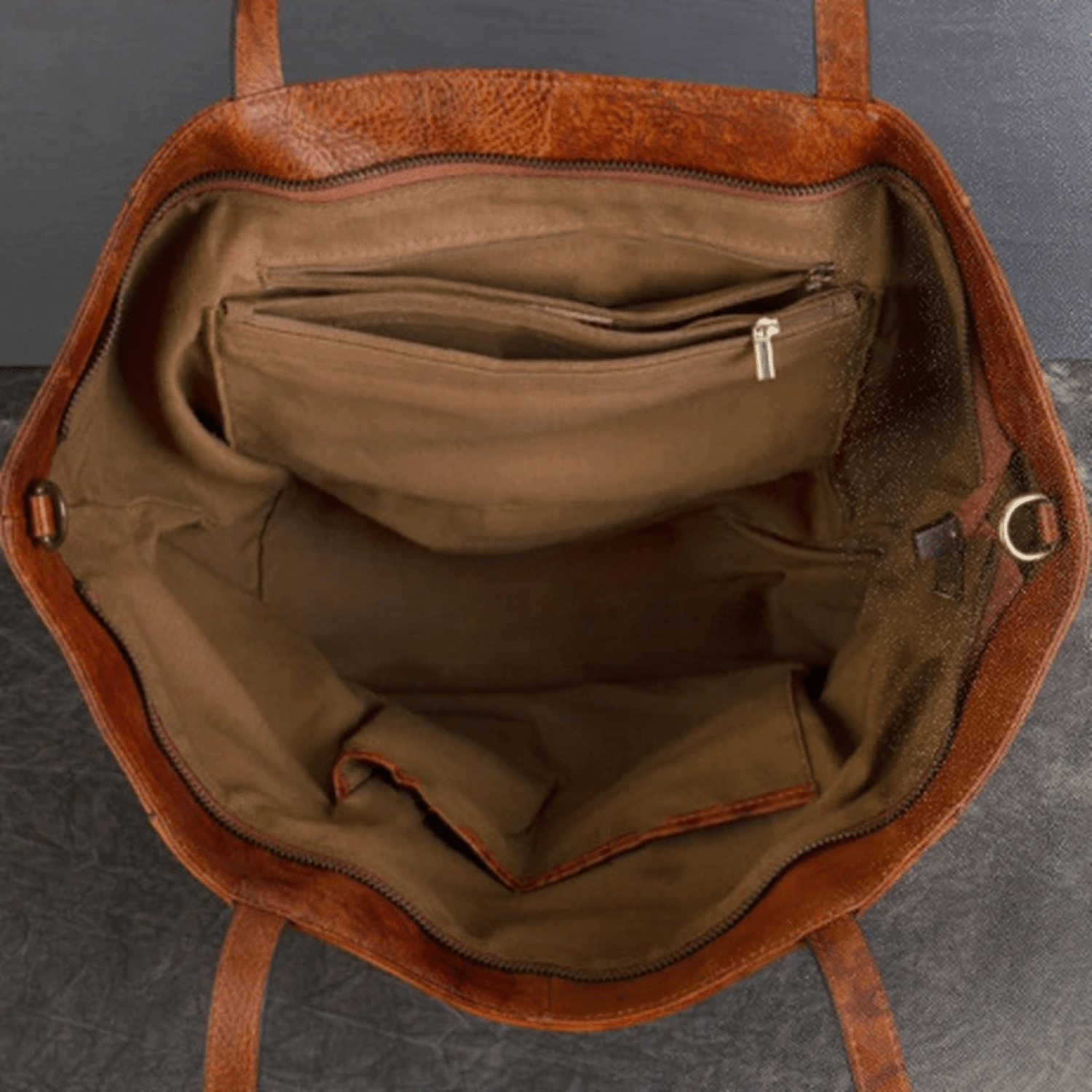 Brown leather handbag with open interior on a gray background