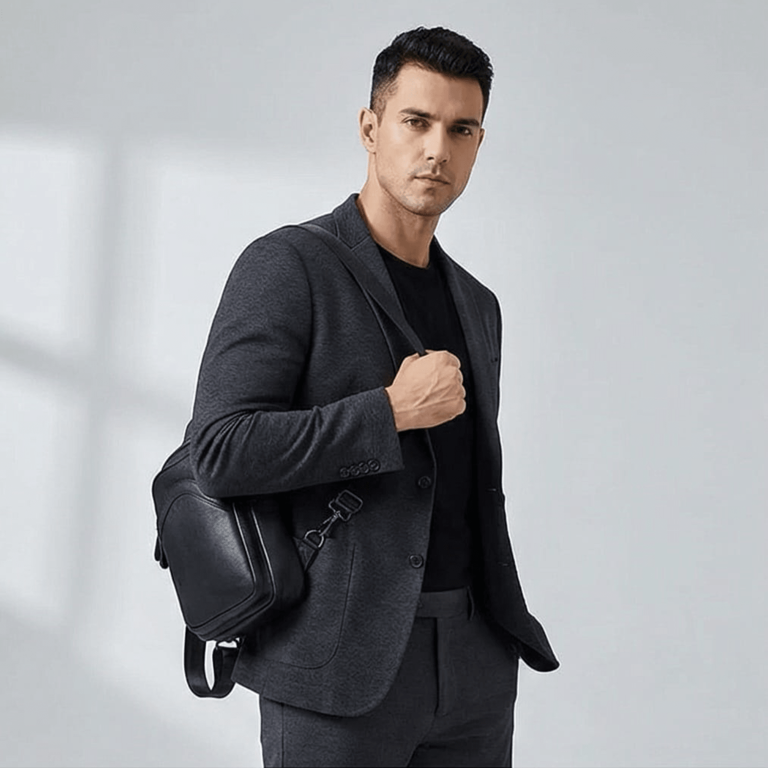 Man in a gray suit holding a black leather bag against a light gray background