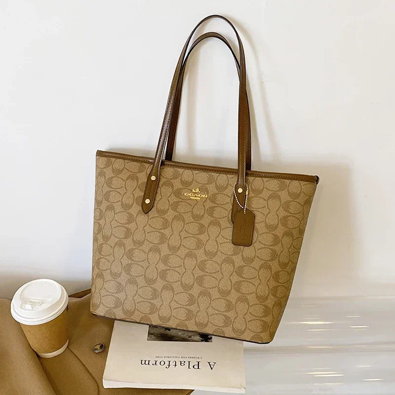 Beige handbag with brown handles and accents on a white surface with a coffee cup and magazine.