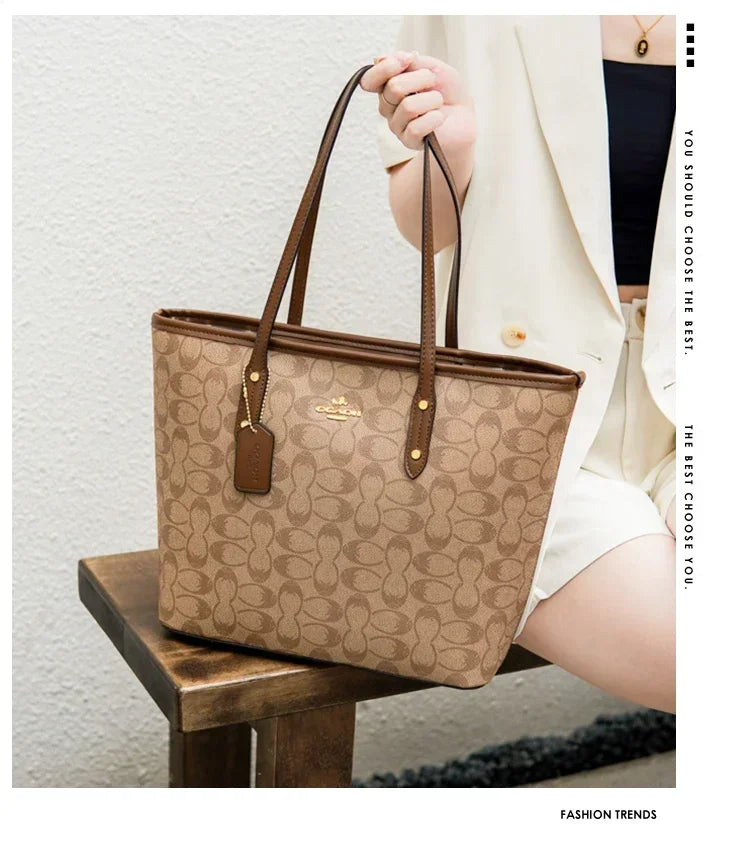 Beige handbag with brown handles held by a person against a neutral background