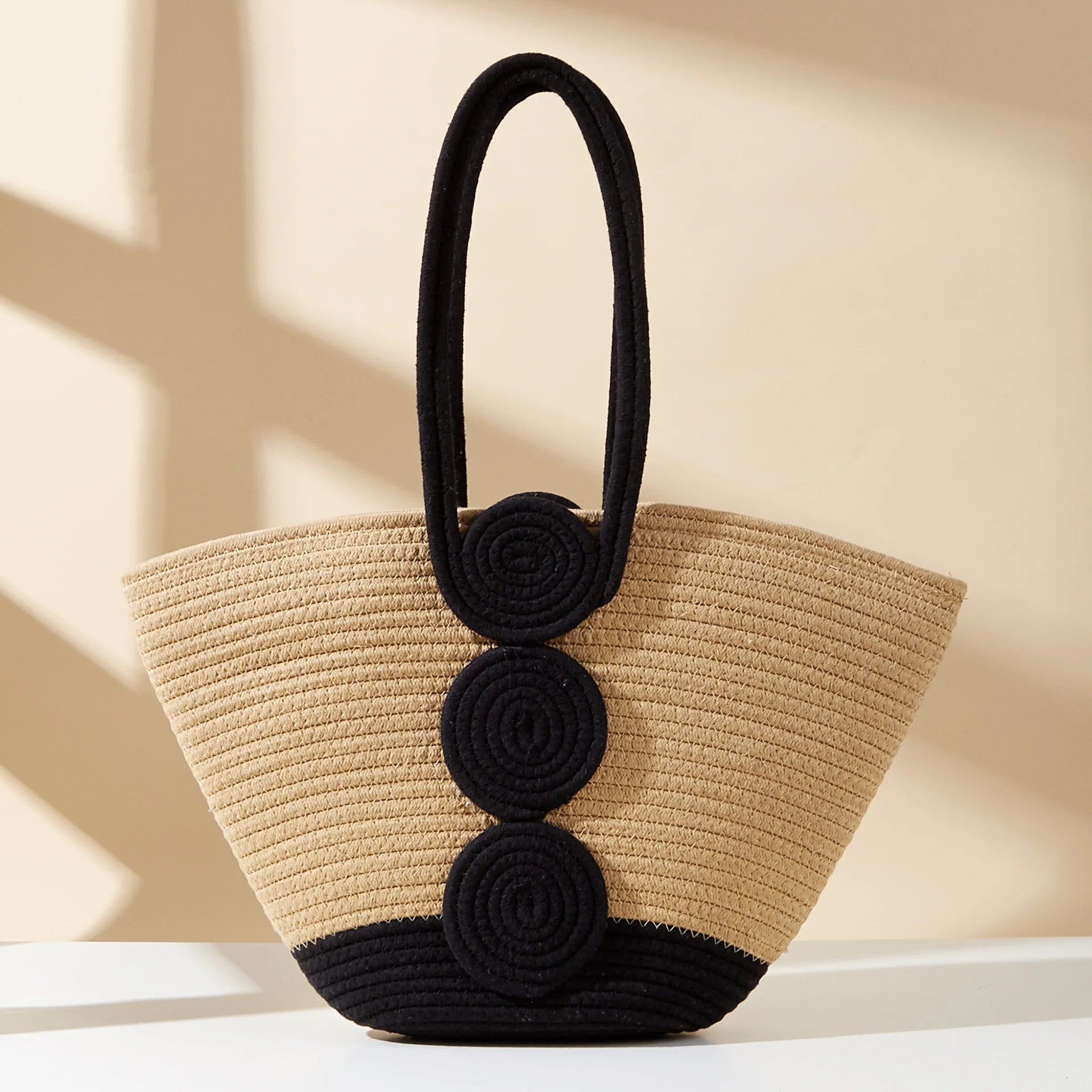 Beige straw handbag with black circular accents on a beige background