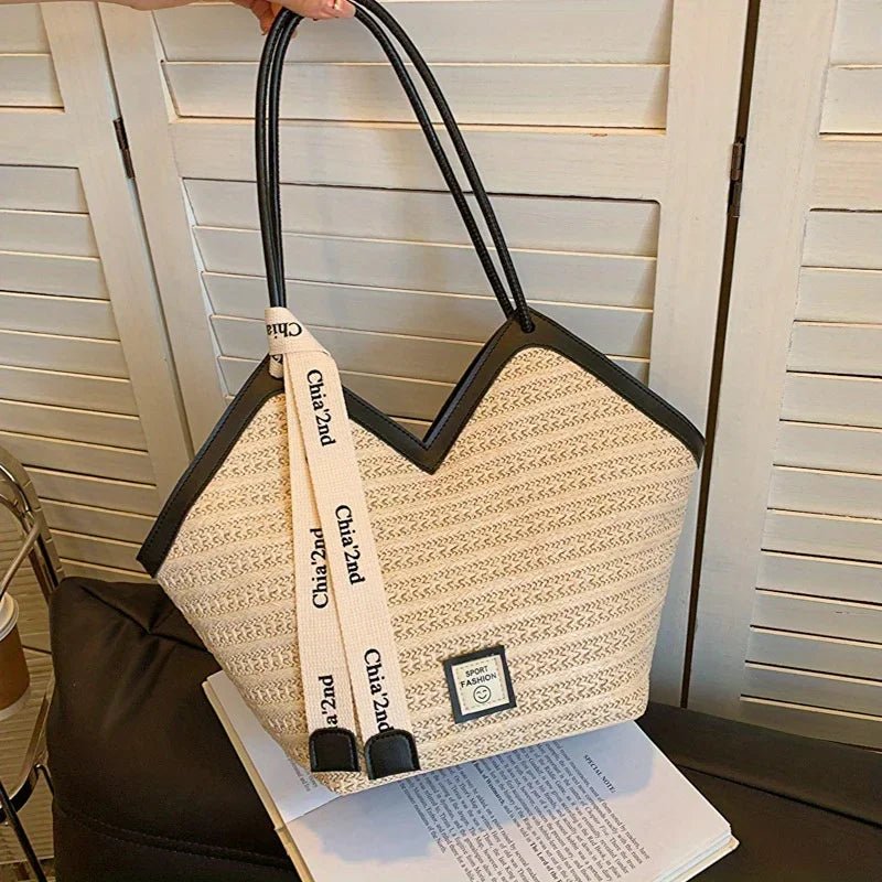 Beige tote bag with black handles and strap on an open book, against a neutral background.
