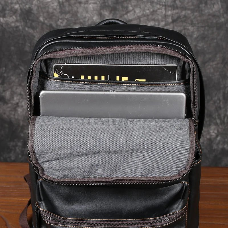 Black backpack with compartments containing a laptop and books on a wooden surface.