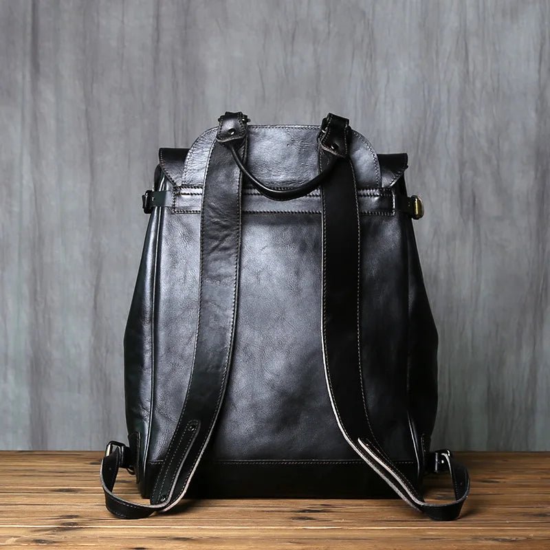 Black leather backpack on a wooden surface with a gray textured background