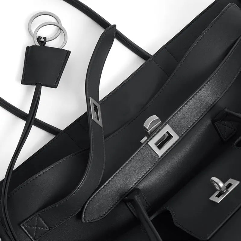 Black leather bag with strap and keychain on a white background