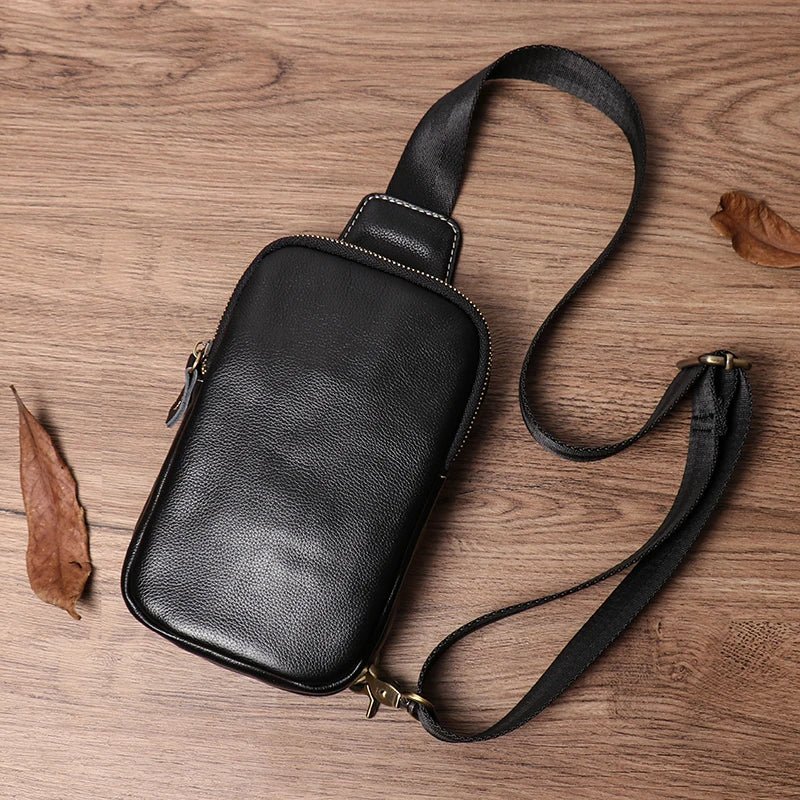 Black leather crossbody bag on a wooden surface with leaves.