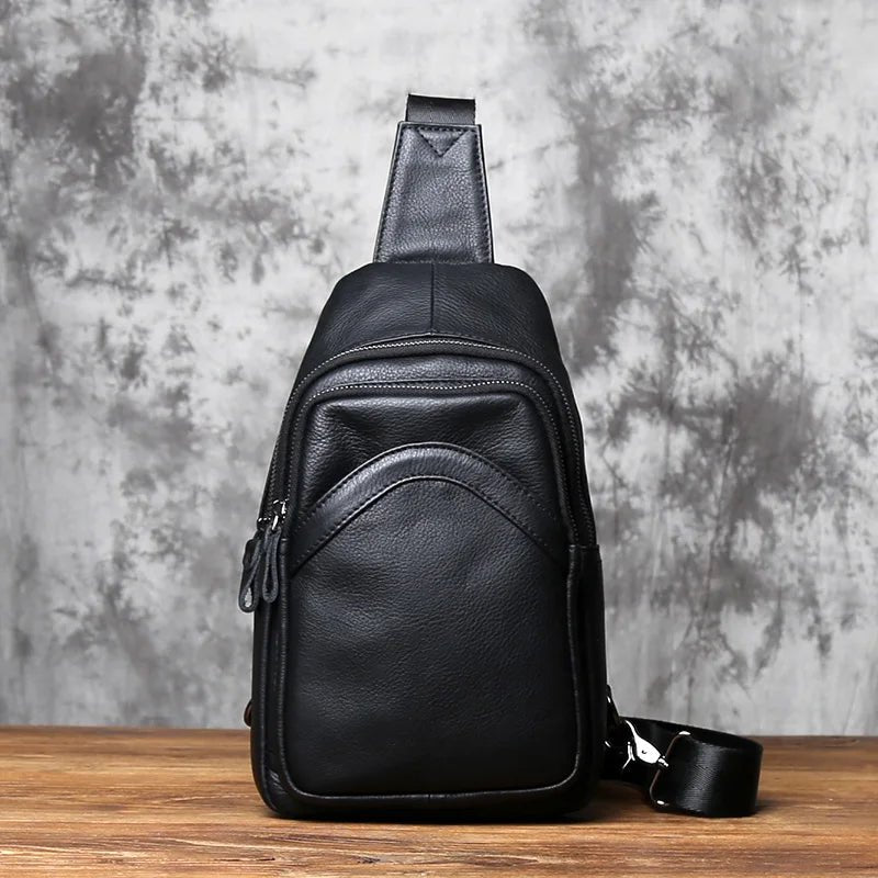 Black leather sling bag on a wooden surface with a gray textured background