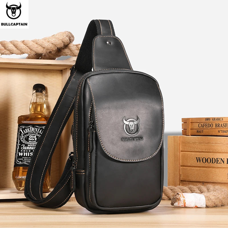 Black leather sling bag with Bullcaptain logo on a wooden surface with a bottle and boxes in the background.