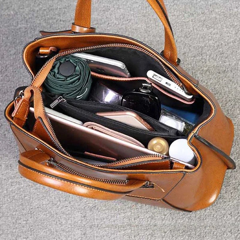 Brown leather handbag with its compartments open, showing various items inside.