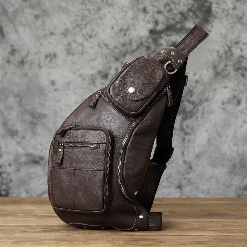 Brown leather sling bag on a wooden surface with a gray marble background