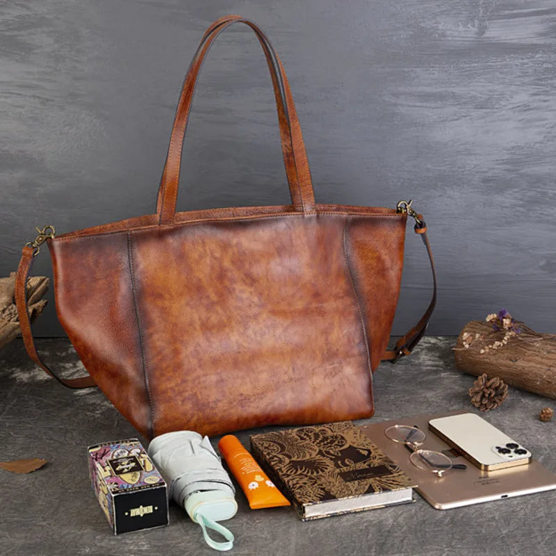 Brown leather tote bag on a gray surface with various items around