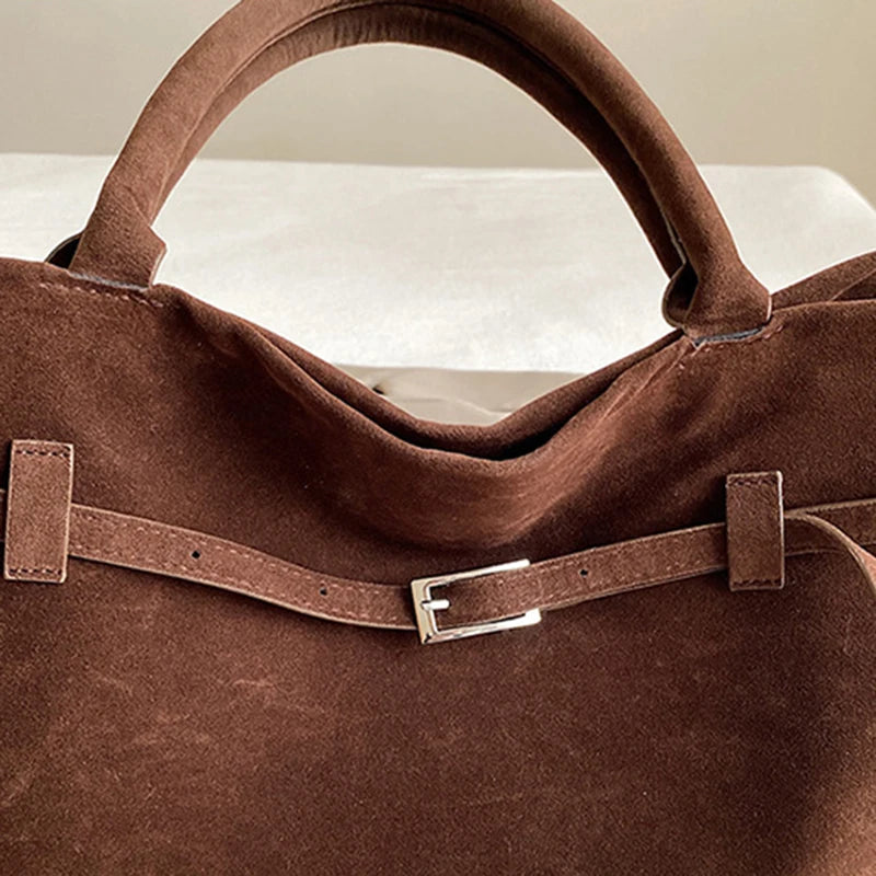 Brown suede handbag with a buckle on a neutral background