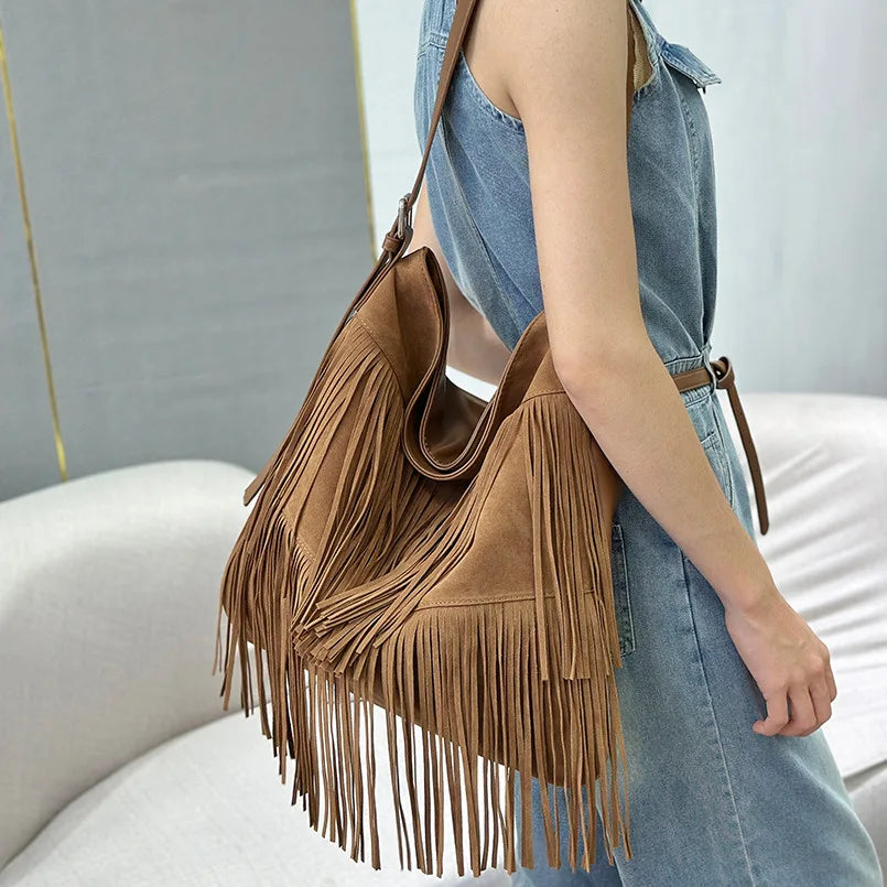 Brown suede handbag with fringe held by a person wearing a denim outfit.