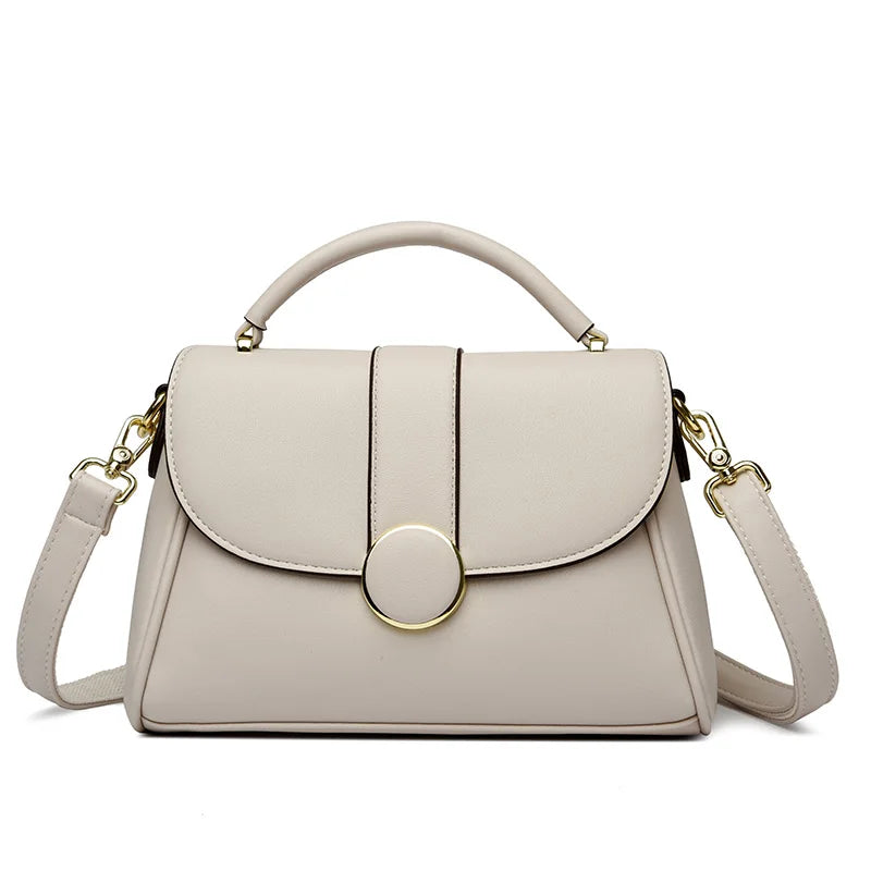 Light beige luxury leather handbag with a structured shape, gold-tone circular clasp, and detachable shoulder strap, set against a white background.