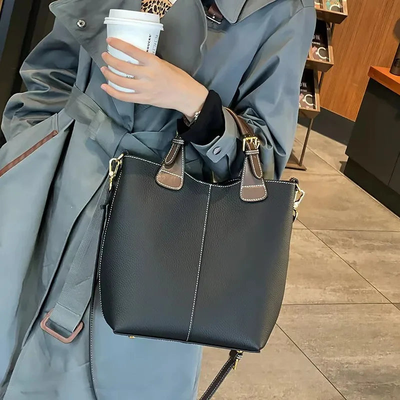 Person holding a black handbag with brown straps and a white cup, wearing a gray coat.