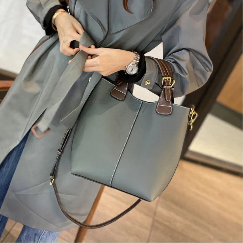 Person holding a large gray handbag with brown accents indoors