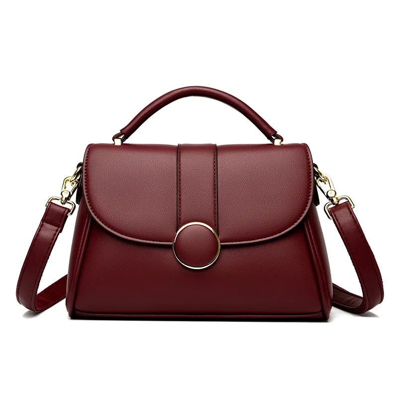 Red luxury leather handbag with a structured shape, gold-tone circular clasp, and detachable shoulder strap, set against a white background.