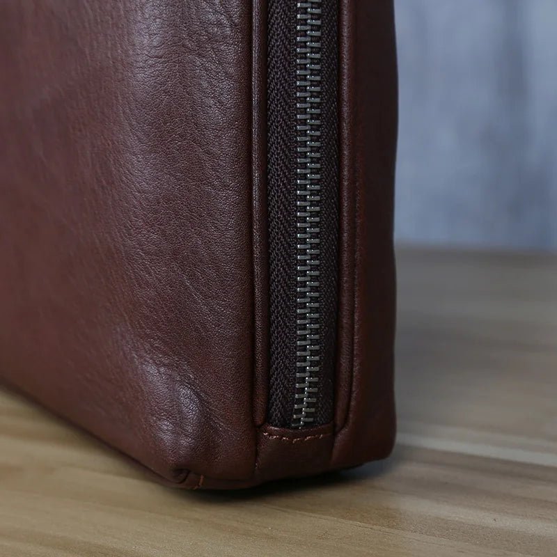 Close-up of a brown leather bag with a zipper on a wooden surface.