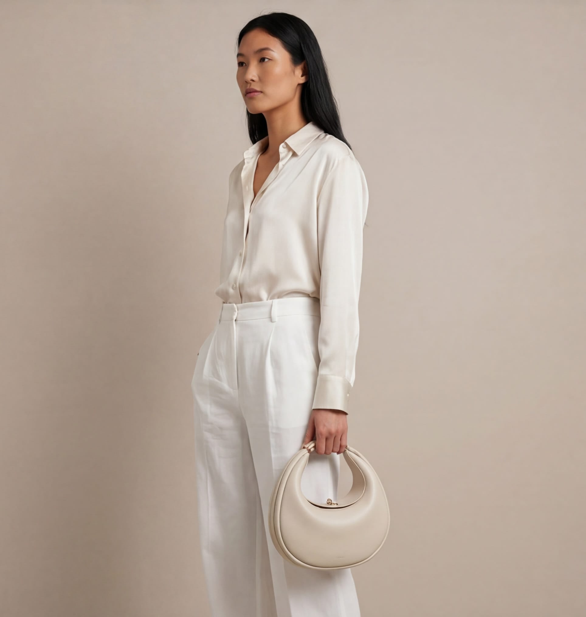 Woman in a white outfit holding a beige handbag against a beige background