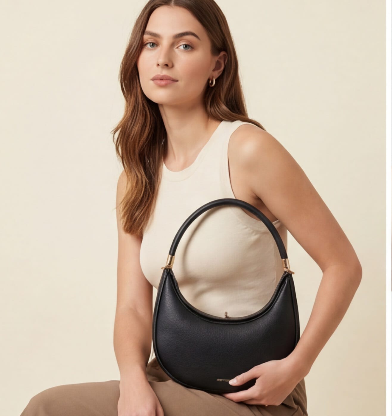 Woman holding a black handbag against a beige background