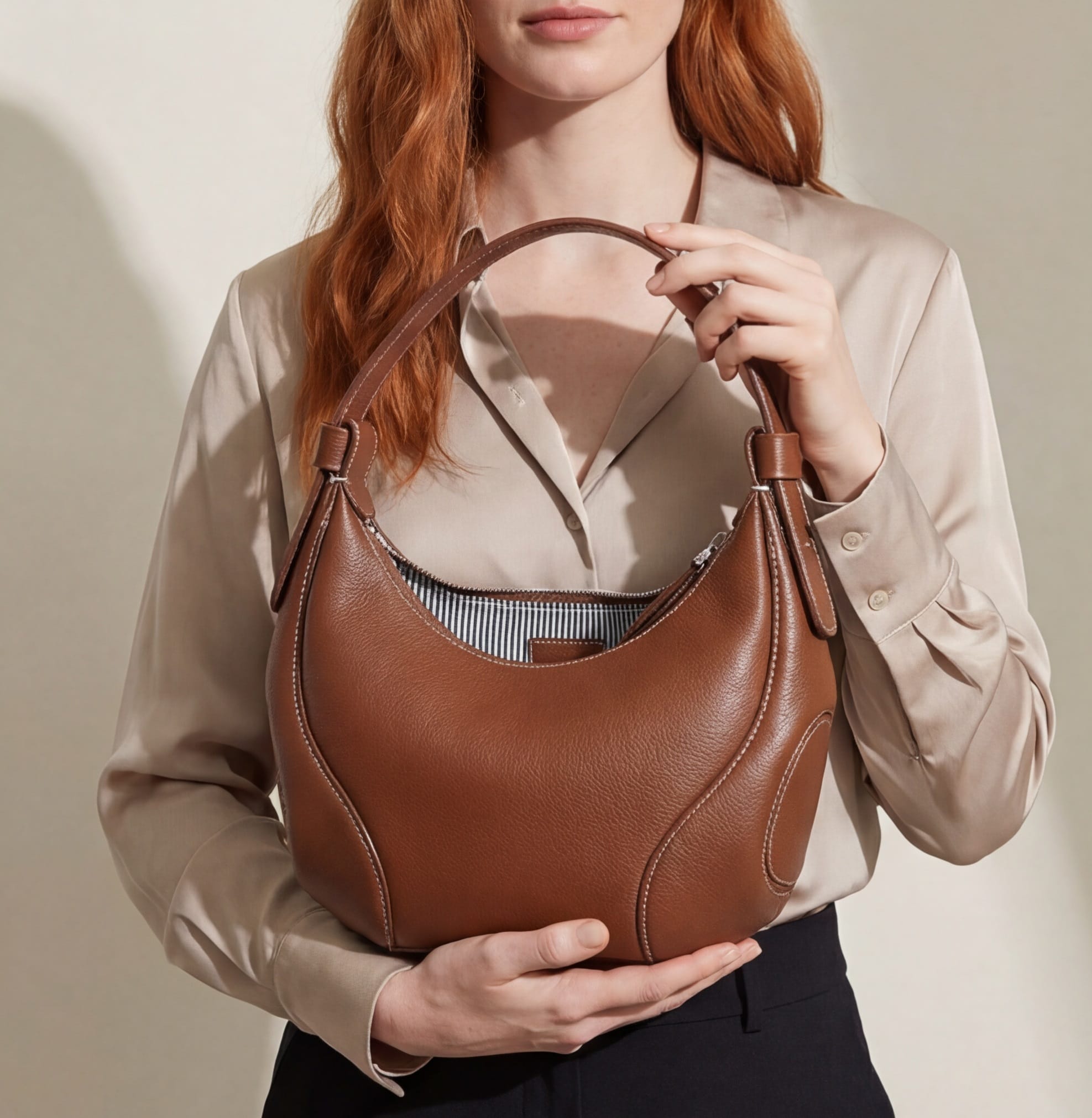 Person holding a brown leather handbag against a neutral background