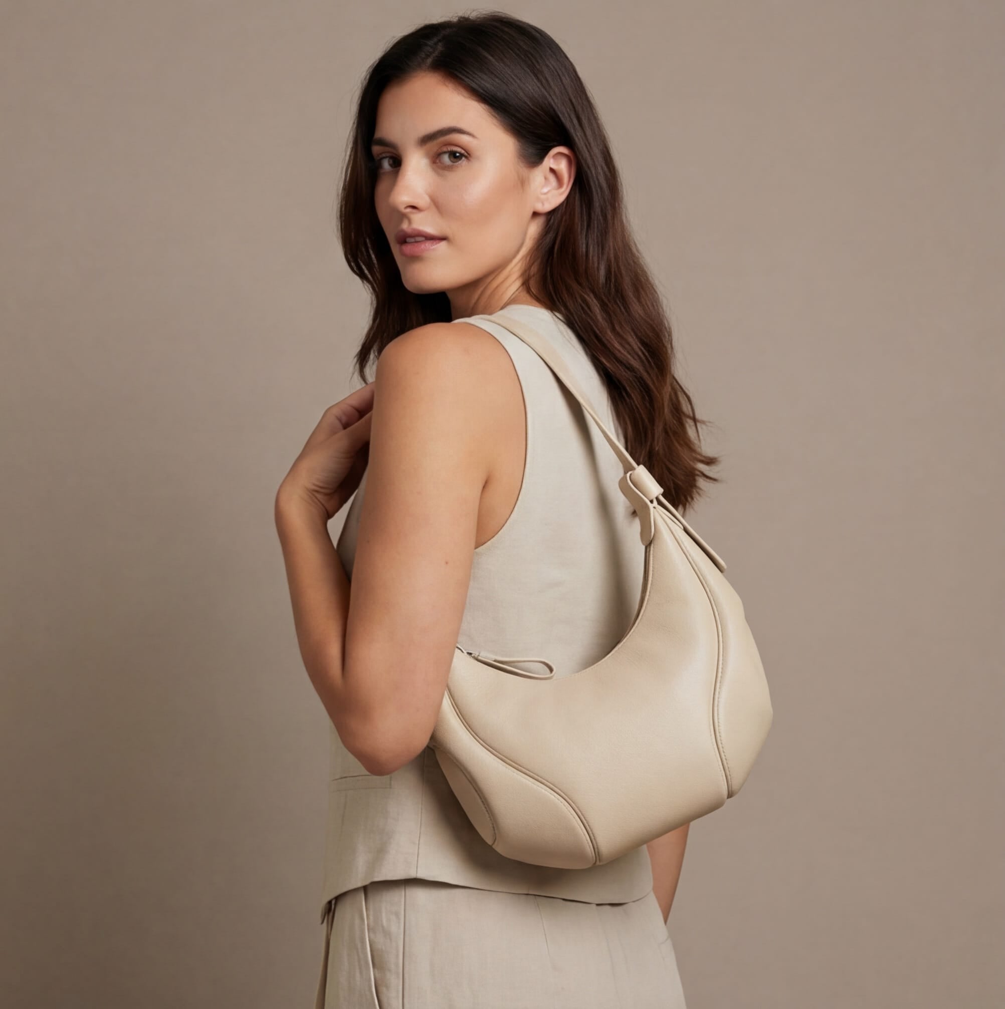 Woman holding a beige handbag against a plain background