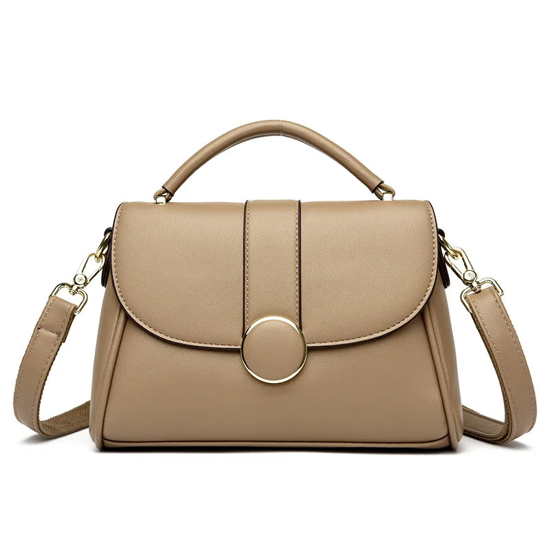 Beige luxury leather handbag with a structured shape, gold-tone circular clasp, and detachable shoulder strap, set against a white background.