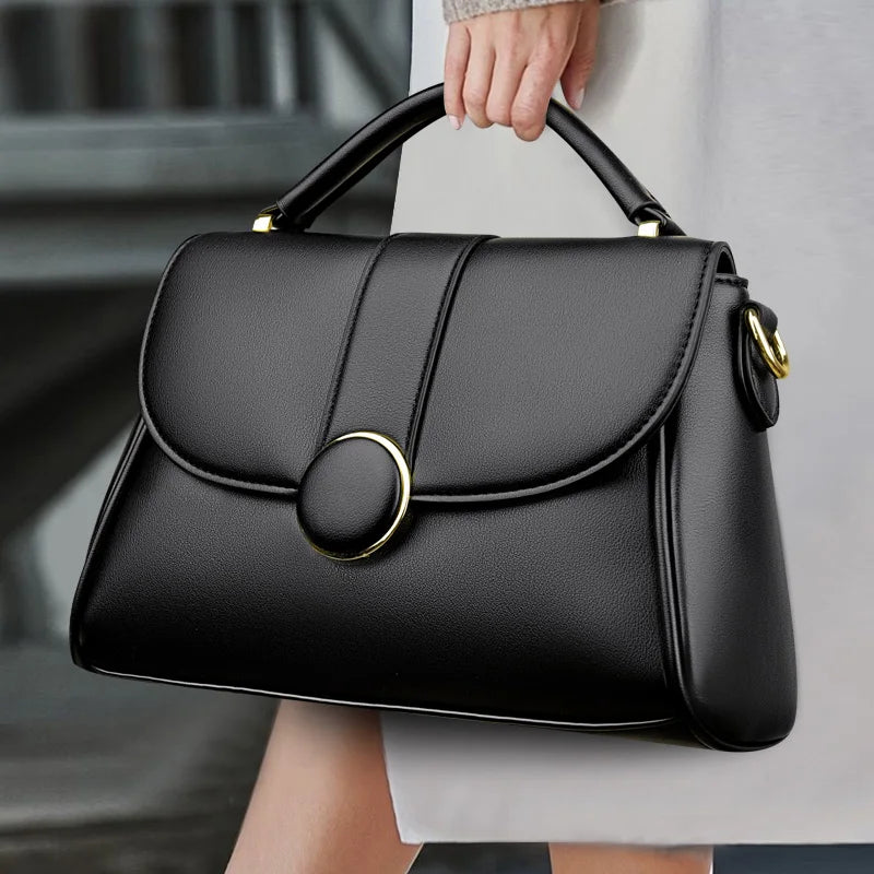 Black luxury leather handbag with gold ring clasp, held by a woman wearing a white outfit.