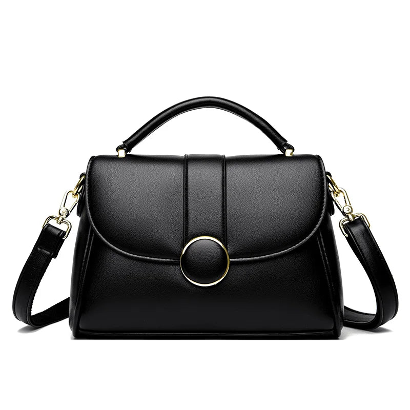 Black luxury leather handbag with a structured shape, gold-tone circular clasp, and detachable shoulder strap, set against a white background.