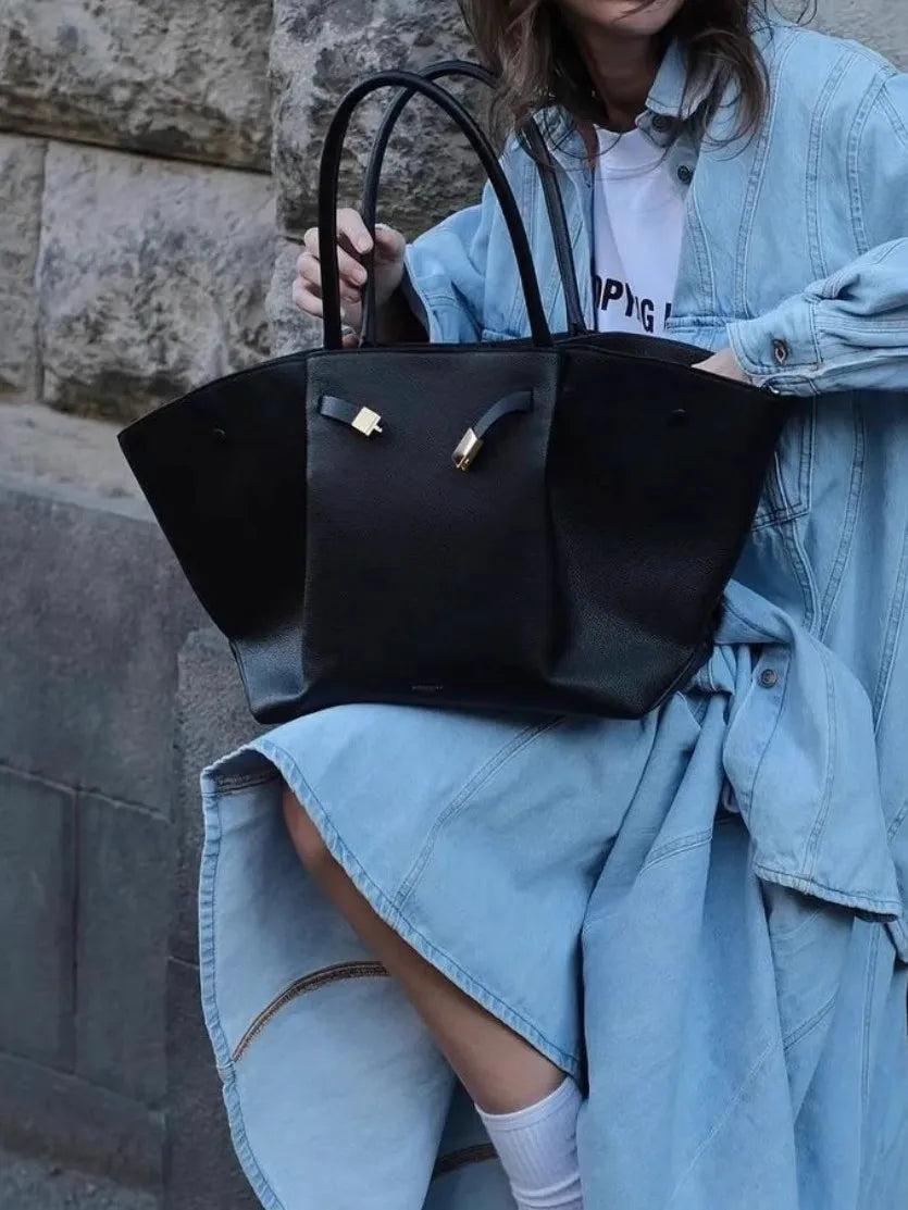 Black suede tote bag held by a woman in a denim outfit