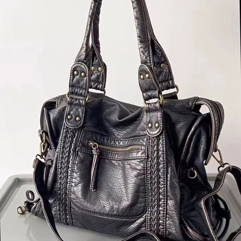 Black vintage Y2K shoulder bag with braided leather details and metal accents, displayed on a reflective surface.