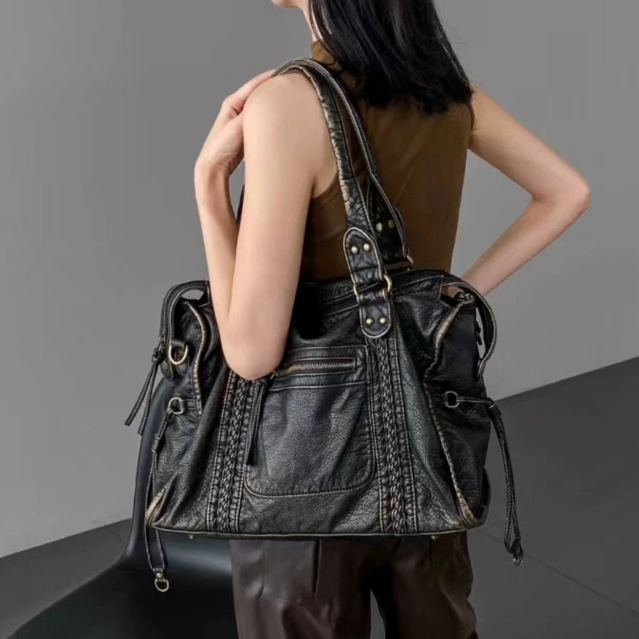 Woman carrying a black Y2K leather shoulder bag on her shoulder, wearing brown leather pants and a sleeveless top.