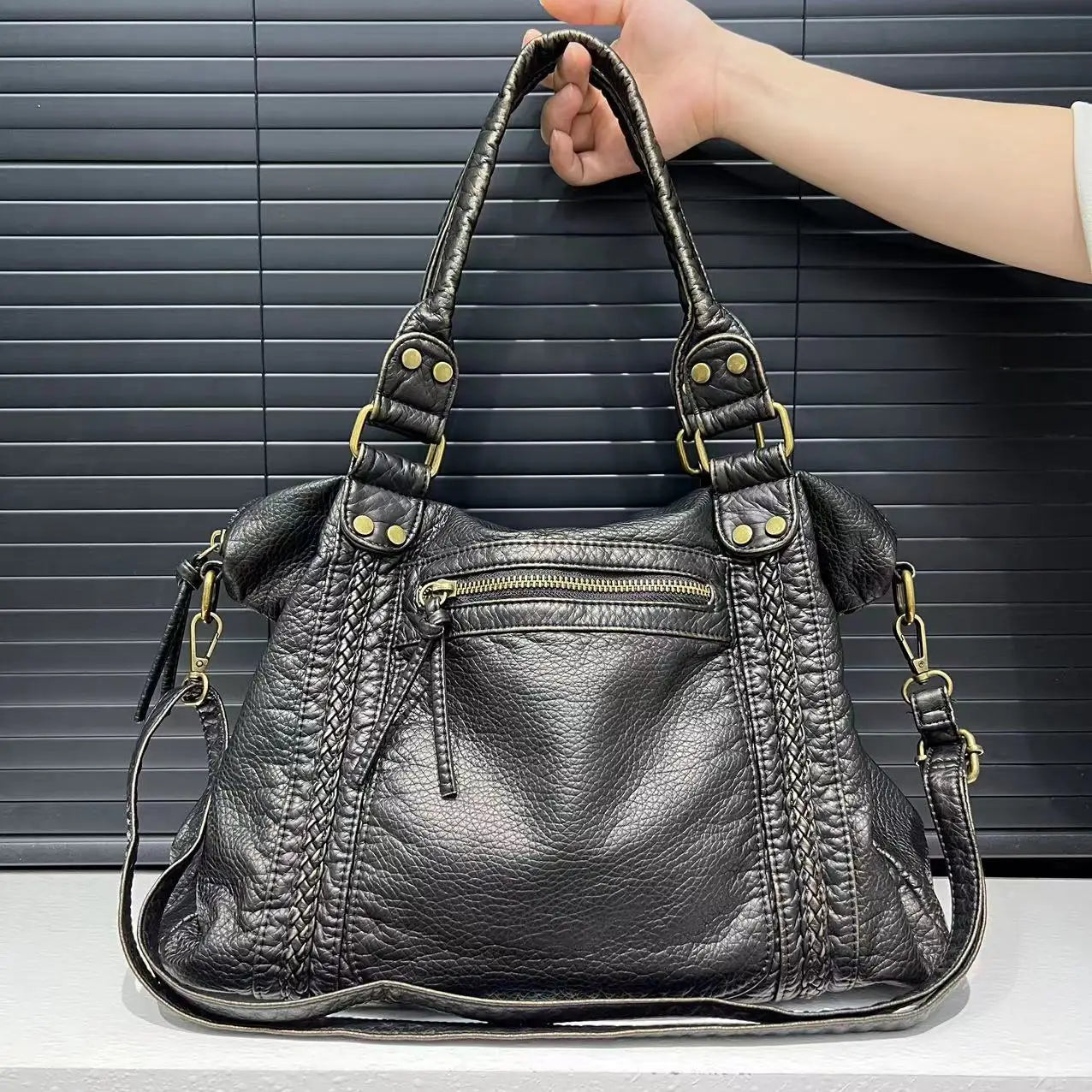 Black vintage Y2K shoulder bag with braided leather details and gold-tone metal accents, held by a hand against a dark background.