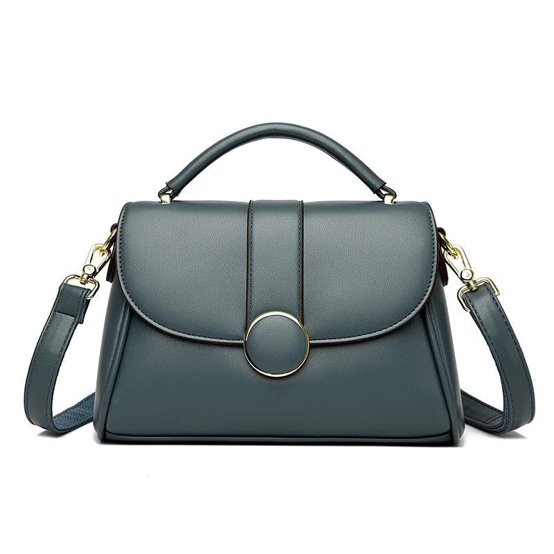 Blue luxury leather handbag with a structured shape, gold-tone circular clasp, and detachable shoulder strap, set against a white background.