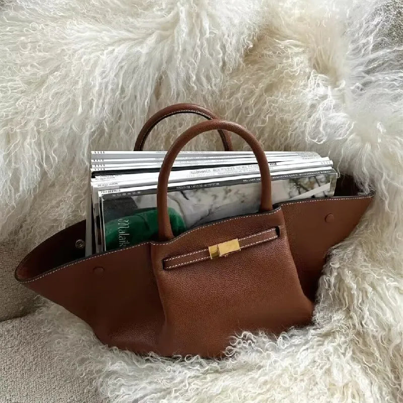 Brown leather tote bag filled with books and essentials on a fluffy surface