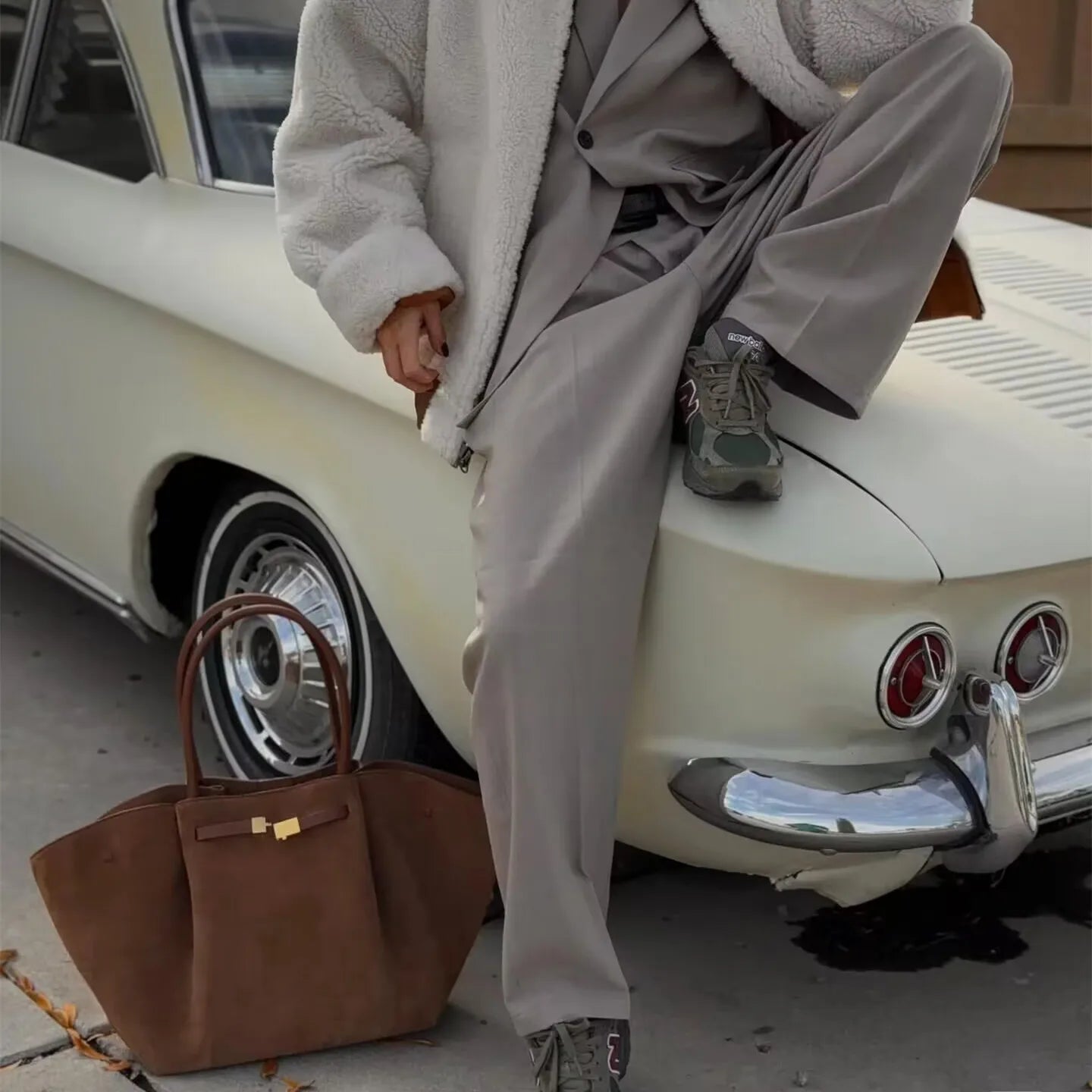 Brown suede tote bag placed on the ground beside a classic car