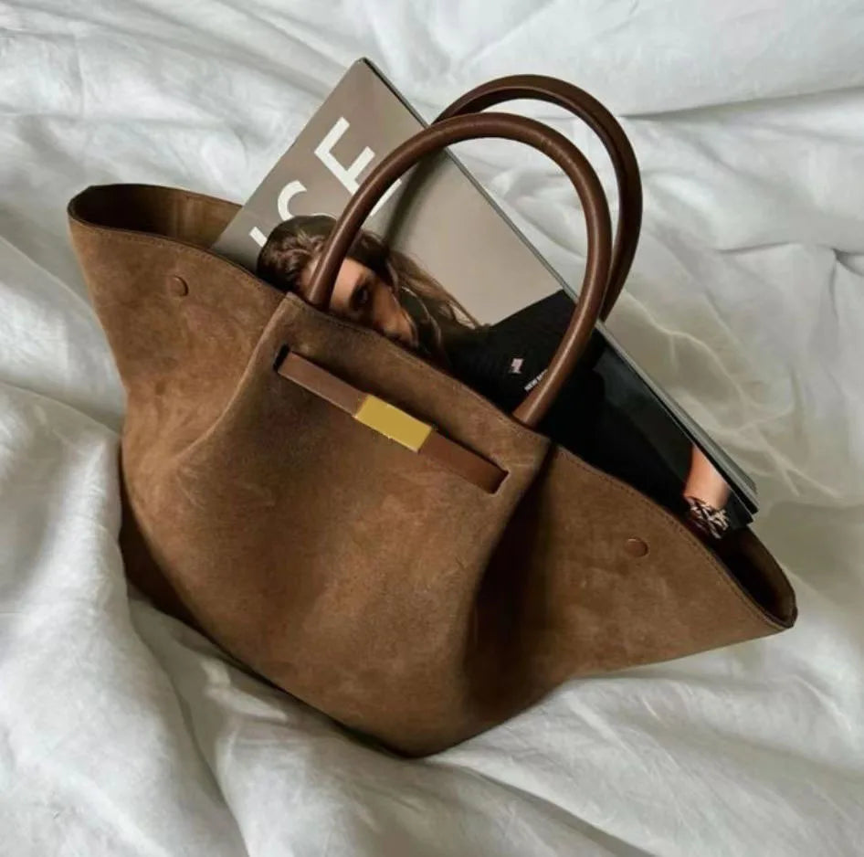 Brown suede tote bag with a magazine inside on a white bed