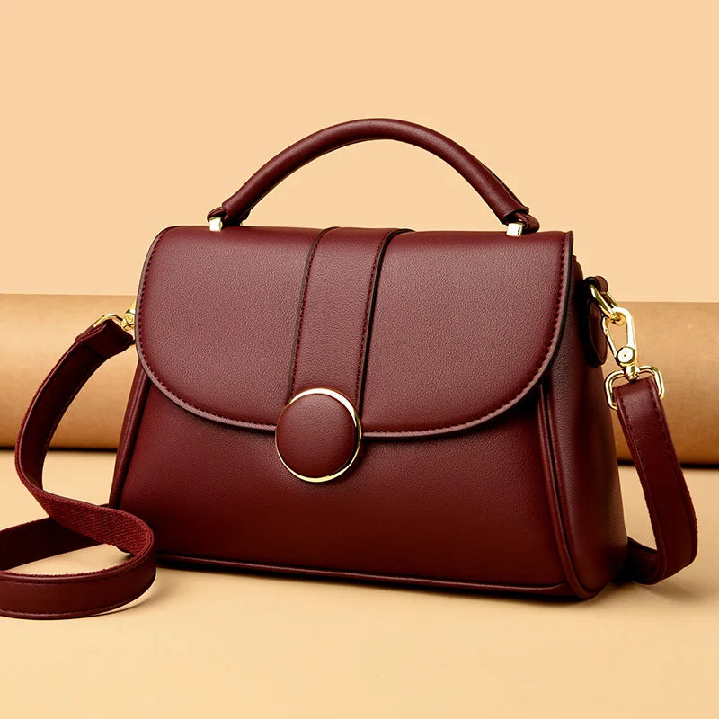 Elegant burgundy leather handbag with a structured design, gold-tone hardware, and a detachable shoulder strap, displayed against a beige background.
