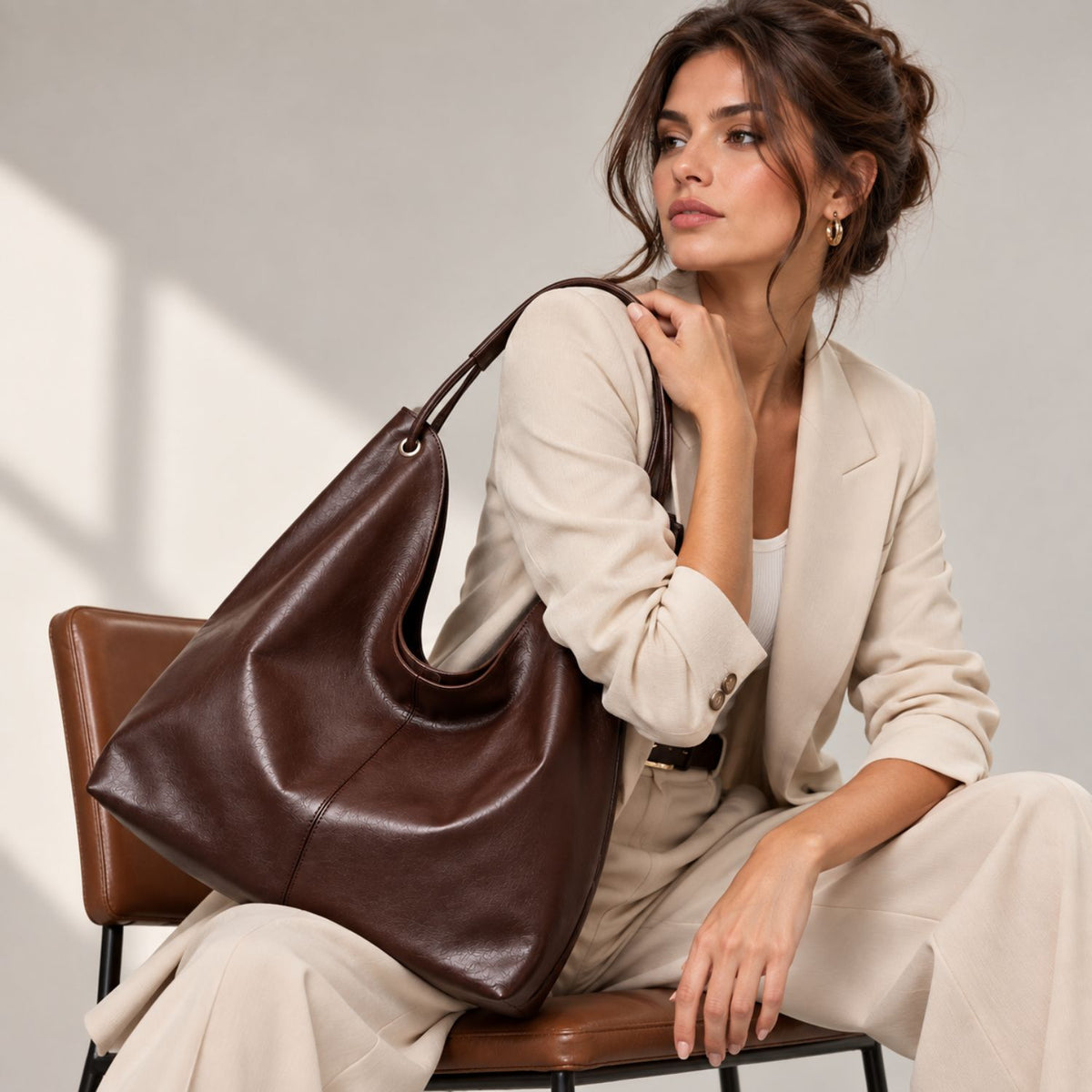 Woman carrying the Daphne brown leather hobo bag with a cream suit