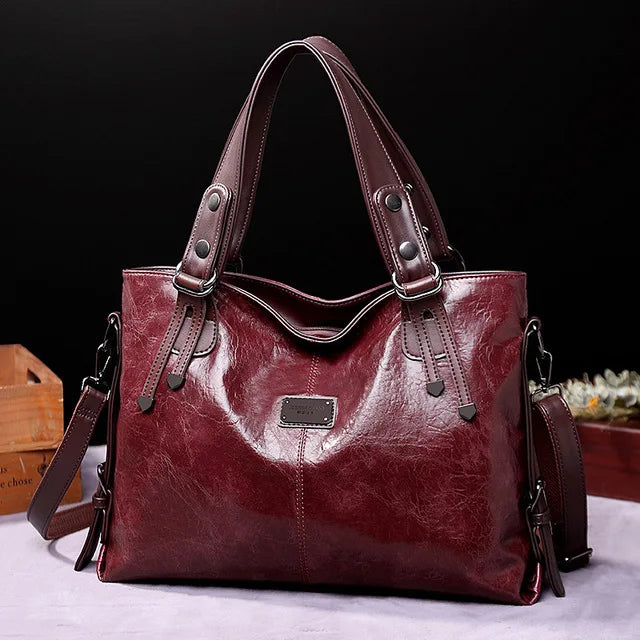 Glossy dark red leather tote bag with brown handles and a detachable shoulder strap, displayed against a black background.