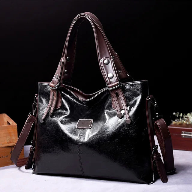 Glossy black leather tote bag with dark brown handles and a detachable shoulder strap, displayed against a black background.