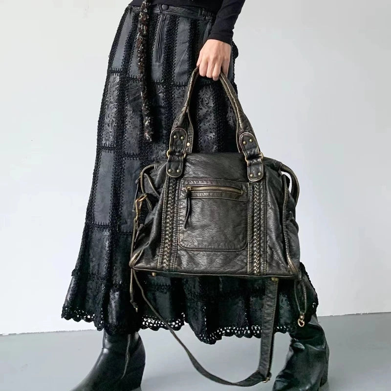 Vintage Y2K black leather handbag with braided details and metal accents, held by a model in a black outfit.