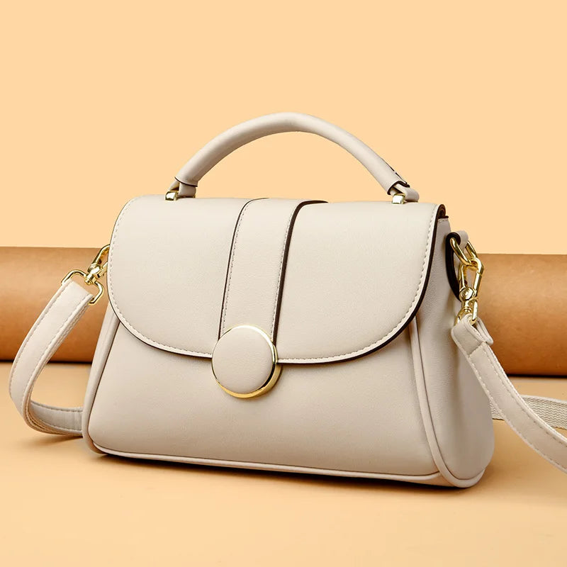 Elegant white leather handbag with a structured design, gold-tone hardware, and a detachable shoulder strap, displayed against a beige background.
