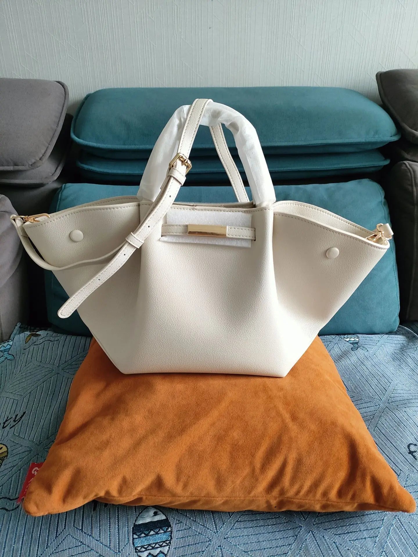White tote bag with a shoulder strap placed on a cushion