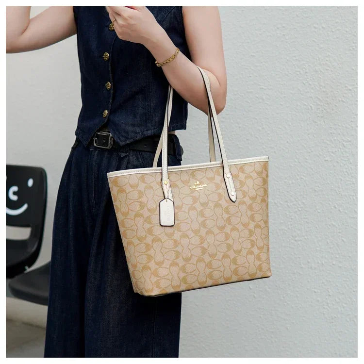Beige handbag with brand logo held by a person against a plain background
