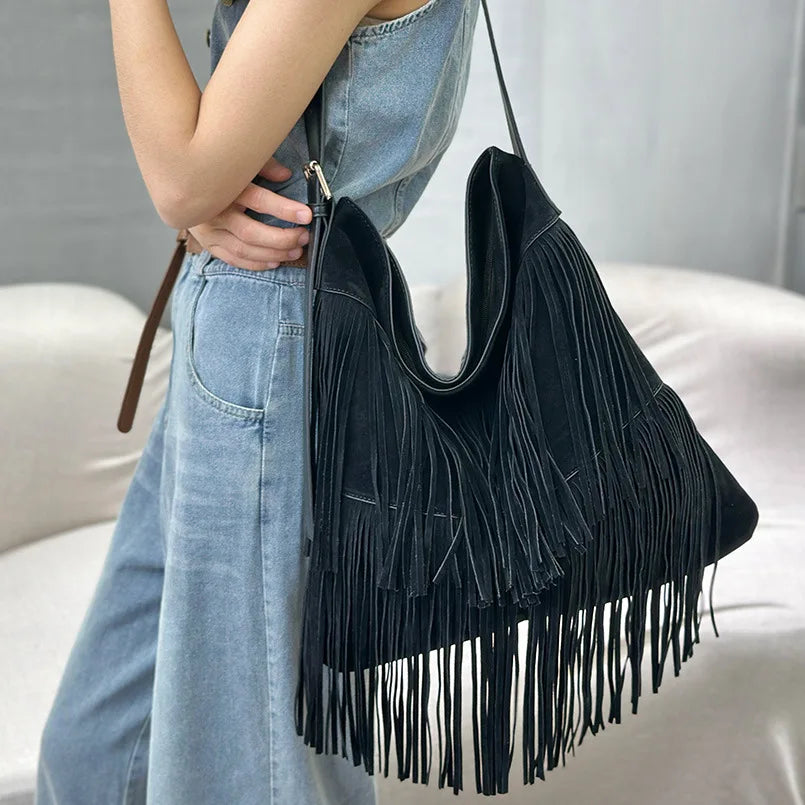 Black fringed handbag held by a person wearing blue jeans against a neutral background