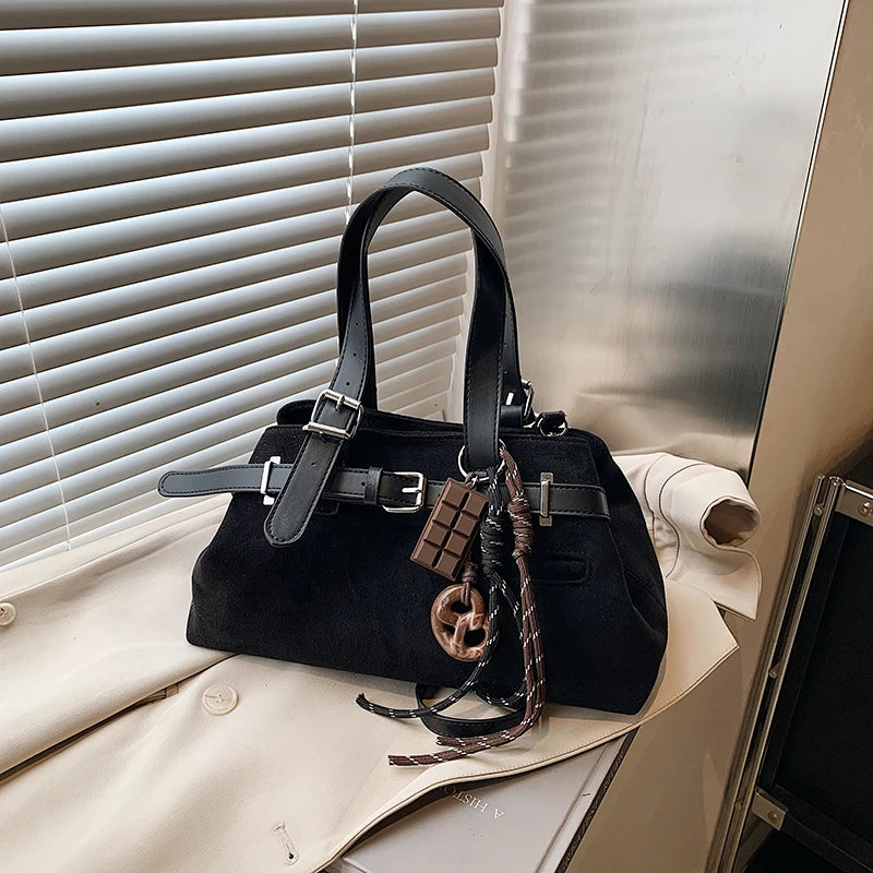 Black handbag with decorative straps on a white surface with blinds in the background