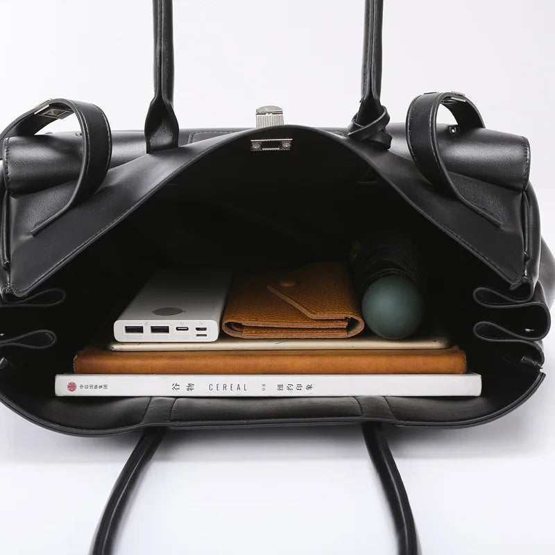 Black leather bag with compartments containing electronic devices and a book on a white background